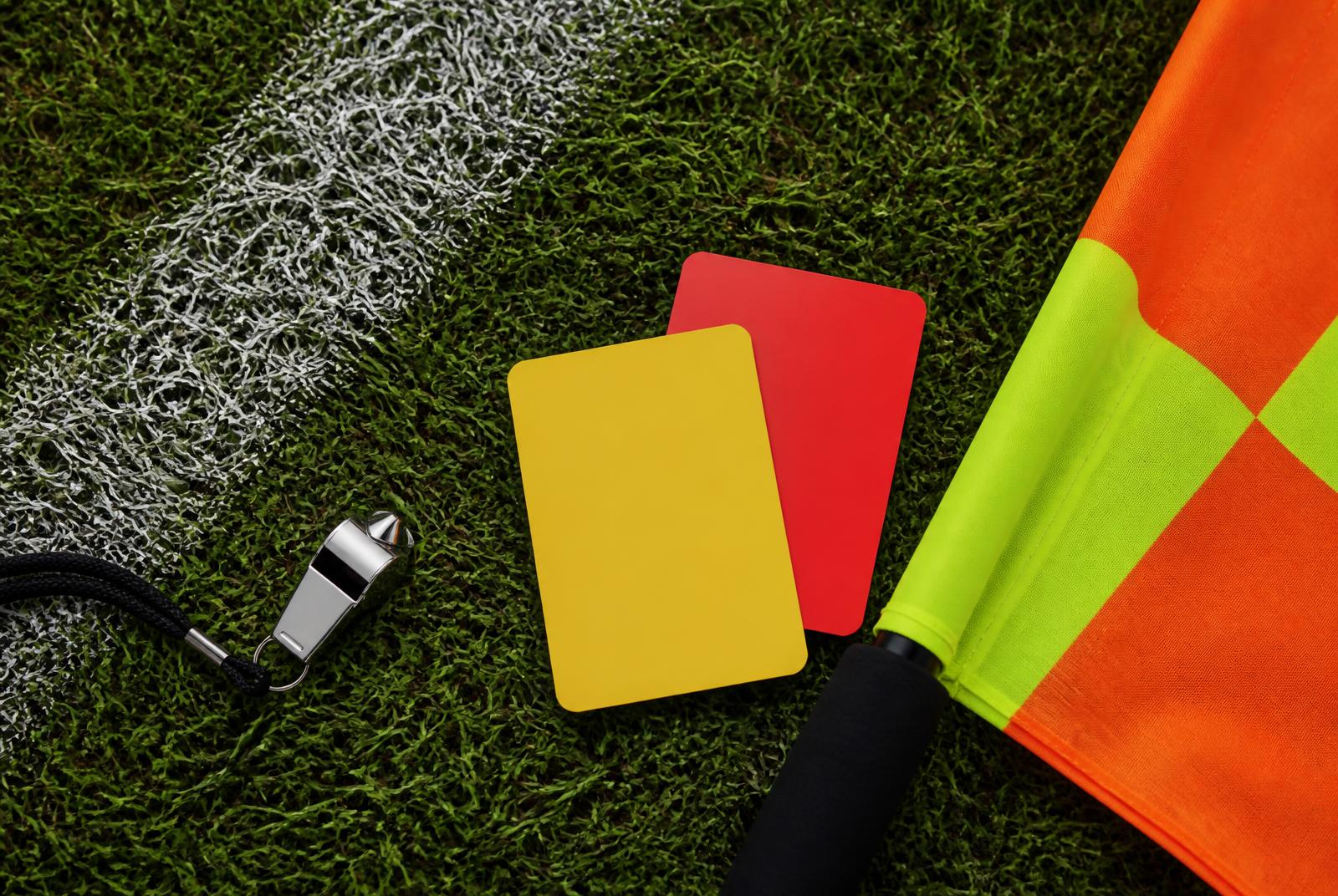 Referee whistle, yellow and red cards, and an assistant referee flag on a grass pitch